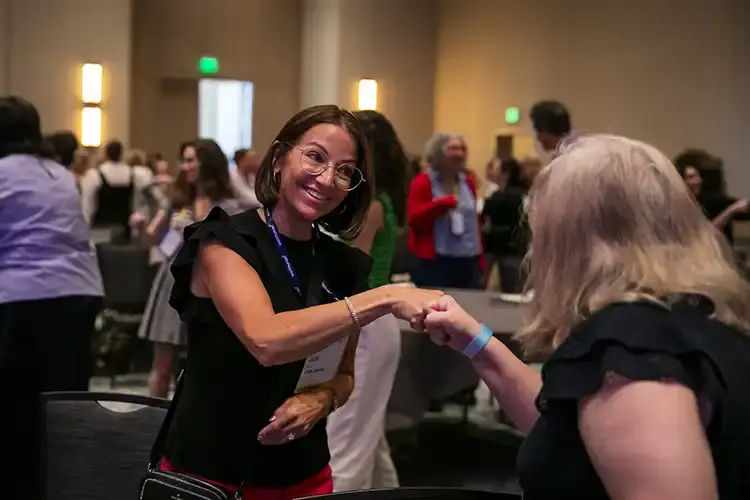 Two attendees of Workhuman Live 2026 give each other a fistbump handshake in the audience of a session.