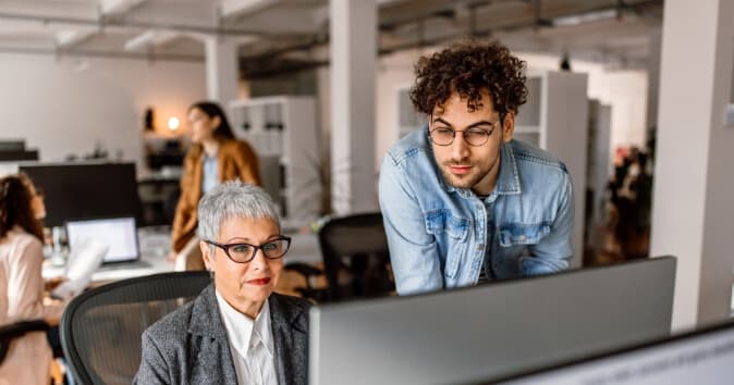 Two people in an office at a desk computer.