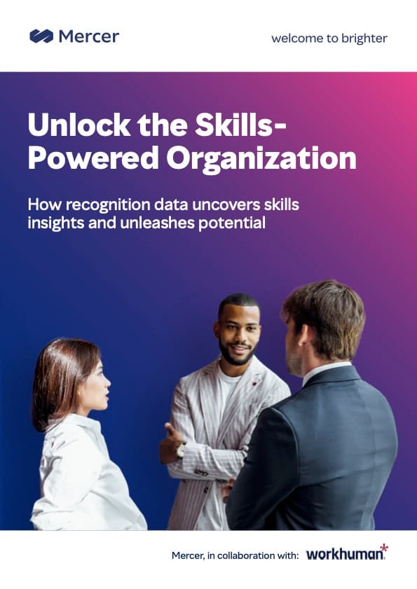 A digital brochure cover from Mercer titled "Unlock the Skills-Powered Organization." The design features a gradient background with three individuals in conversation: a woman with long hair dressed in a white blouse, a man with a striped jacket smiling, and another man in a suit facing the other two. The text highlights how recognition data can uncover skills insights and unleash potential, with a note that the collaboration is with Workhuman.