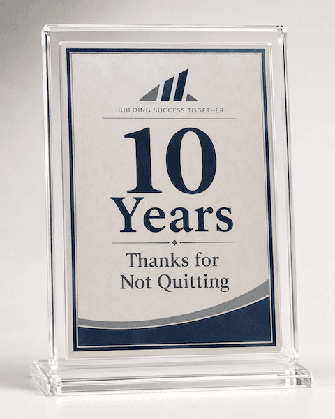 A recognition award displayed on a clear acrylic plaque. The award features the text "BUILDING SUCCESS TOGETHER" at the top, with "10 Years" prominently centered in large font. Below that, the phrase "Thanks for Not Quitting" is written in a smaller font. The award has a simple, elegant design with a blue and cream color scheme.