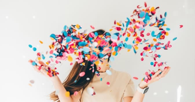 A woman standing behind confetti being thrown in the air.