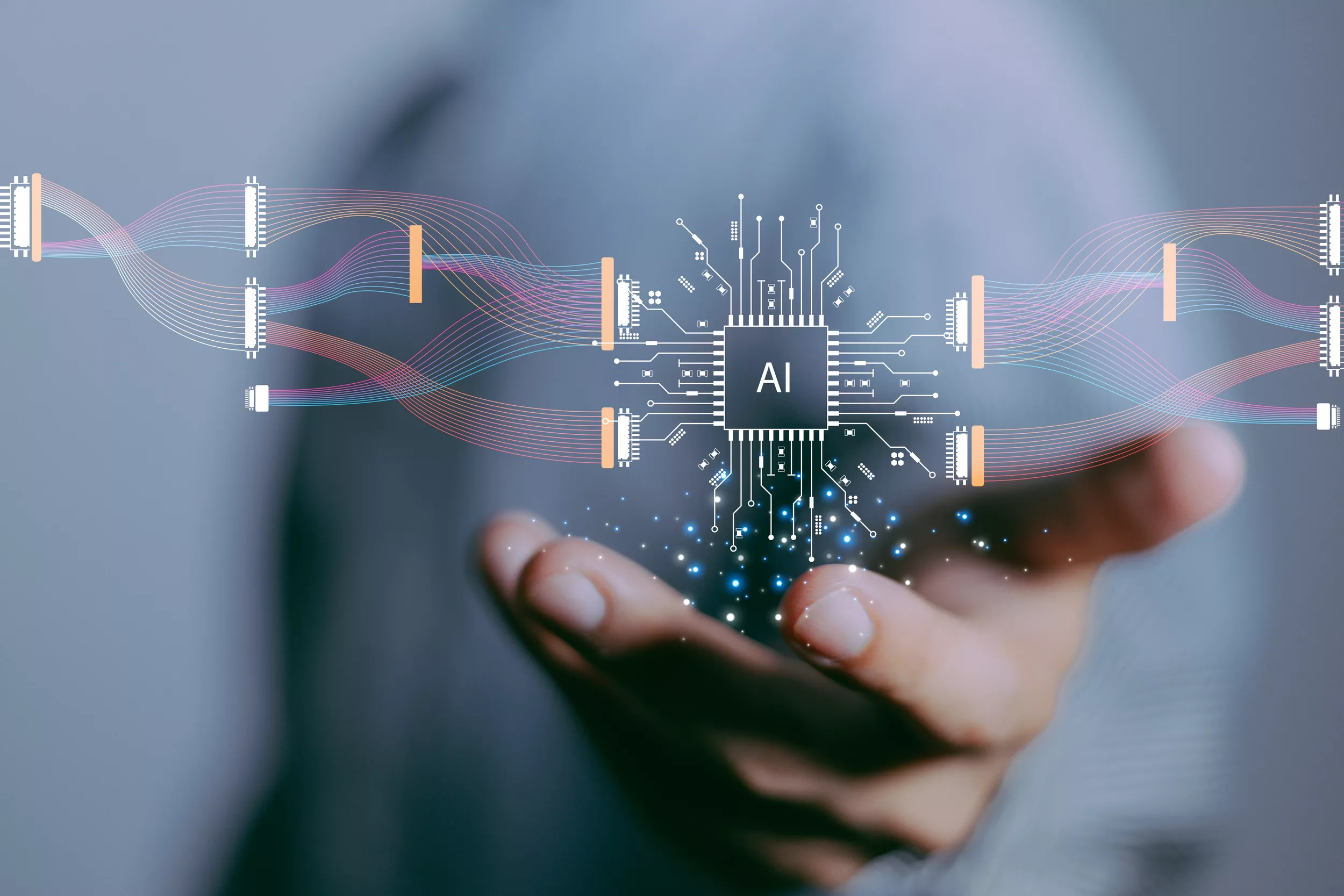 A close-up of a hand reaching out, with a digital representation of a circuit board and an "AI" label in the center. There are various colorful lines and connections emanating from the circuit, suggesting the flow of information or data. The background is softly blurred in a neutral tone, emphasizing the hand and the digital elements in focus.