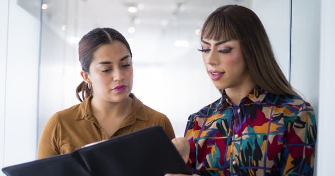 Two people talking looking at a notebook.