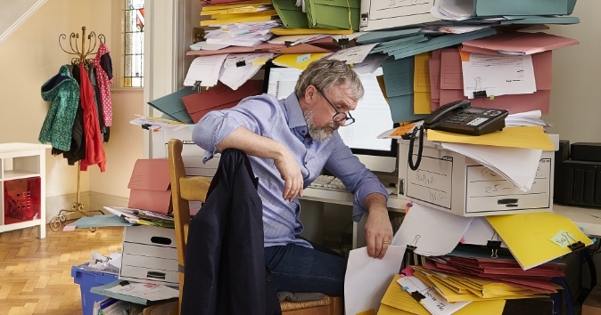 Man at home office with tons of office work and files.
