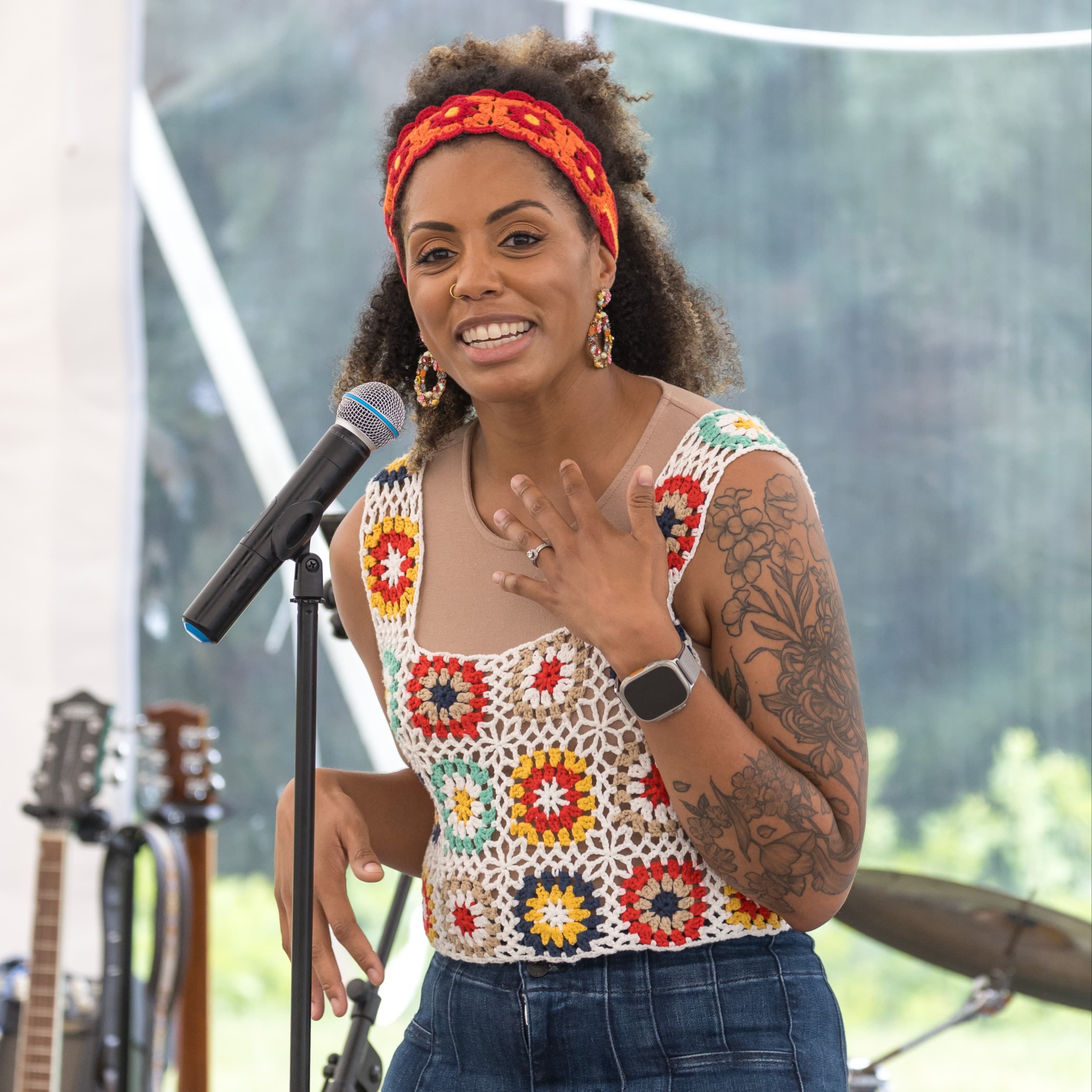 Workhuman employee standing in front of a Mic, at a summer company event. She is smiling widely and looks to be in the middle of preforming. She is dressed in 70's themed clothing.
