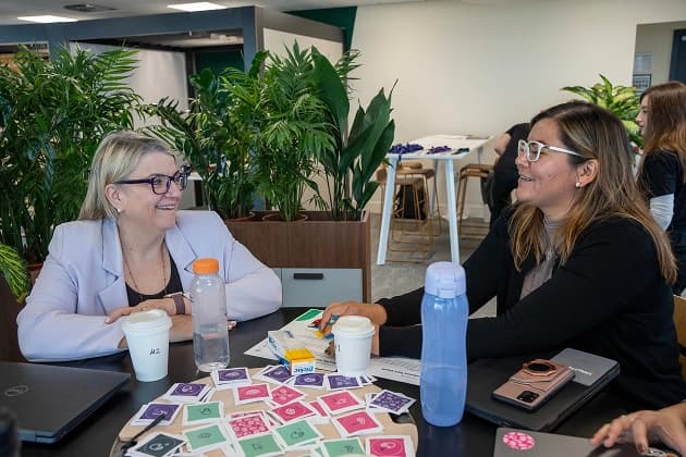 A woman in focus smiling and holding an iPad surrounded by coworkers in conversation.
