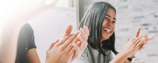 Woman clapping in a room with other people clapping at a table.