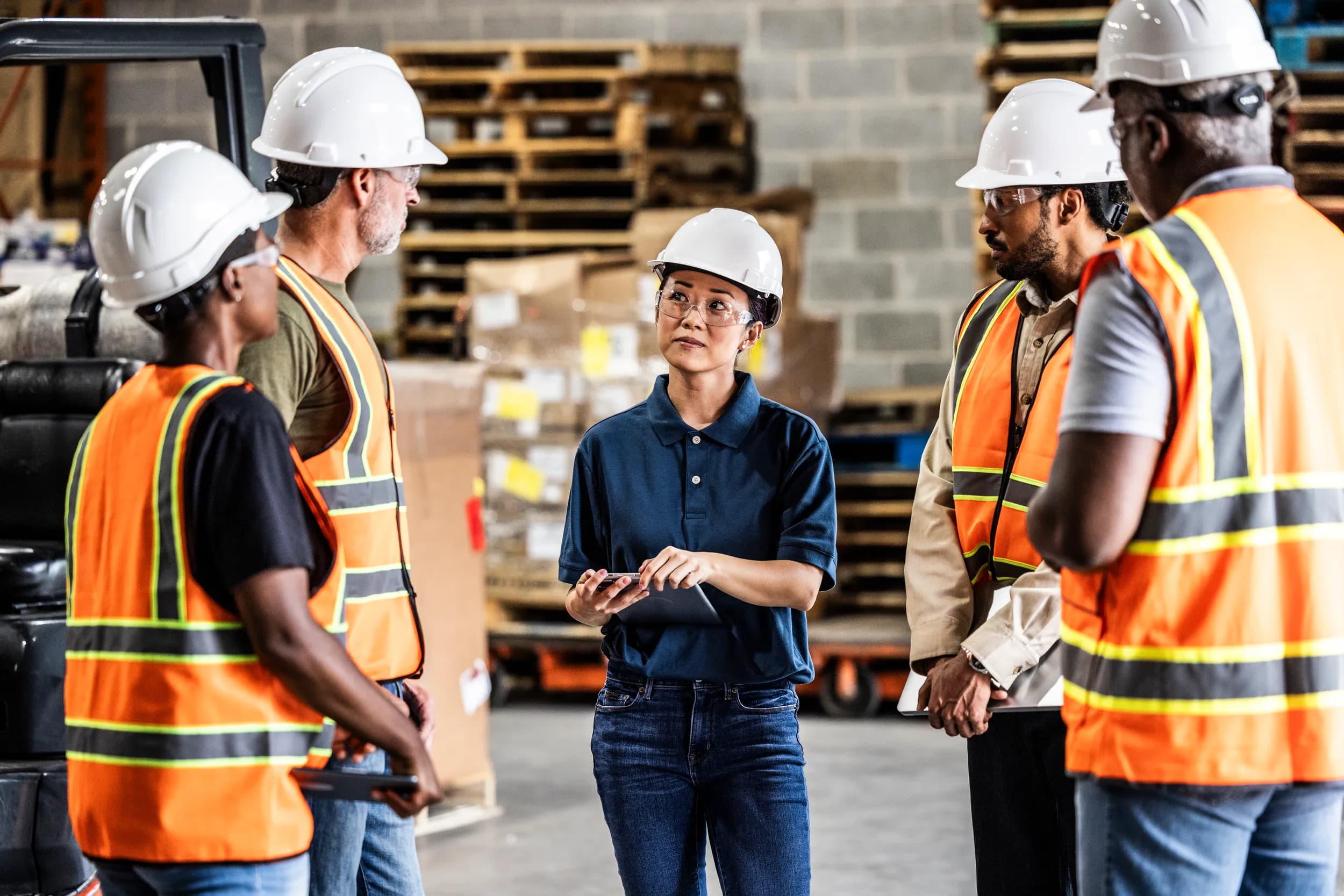 A femaie supervisor meets with four reports in hardhats on a factory floor
