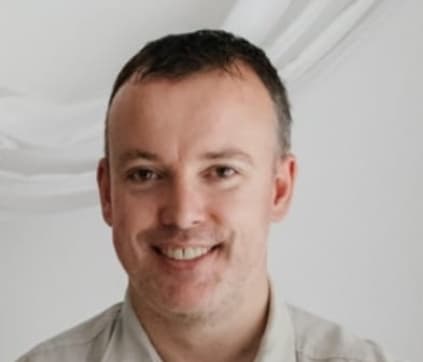 A smiling individual with short hair and a light-colored shirt appears in the image, set against a neutral background. The expression conveys a friendly and approachable demeanor.