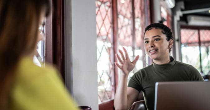 women sitting in front of the laptop and talking to other