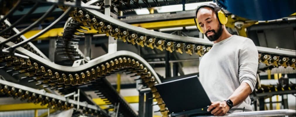 a man wearing protective headphone on a computer on the floor of a manufacturing plant