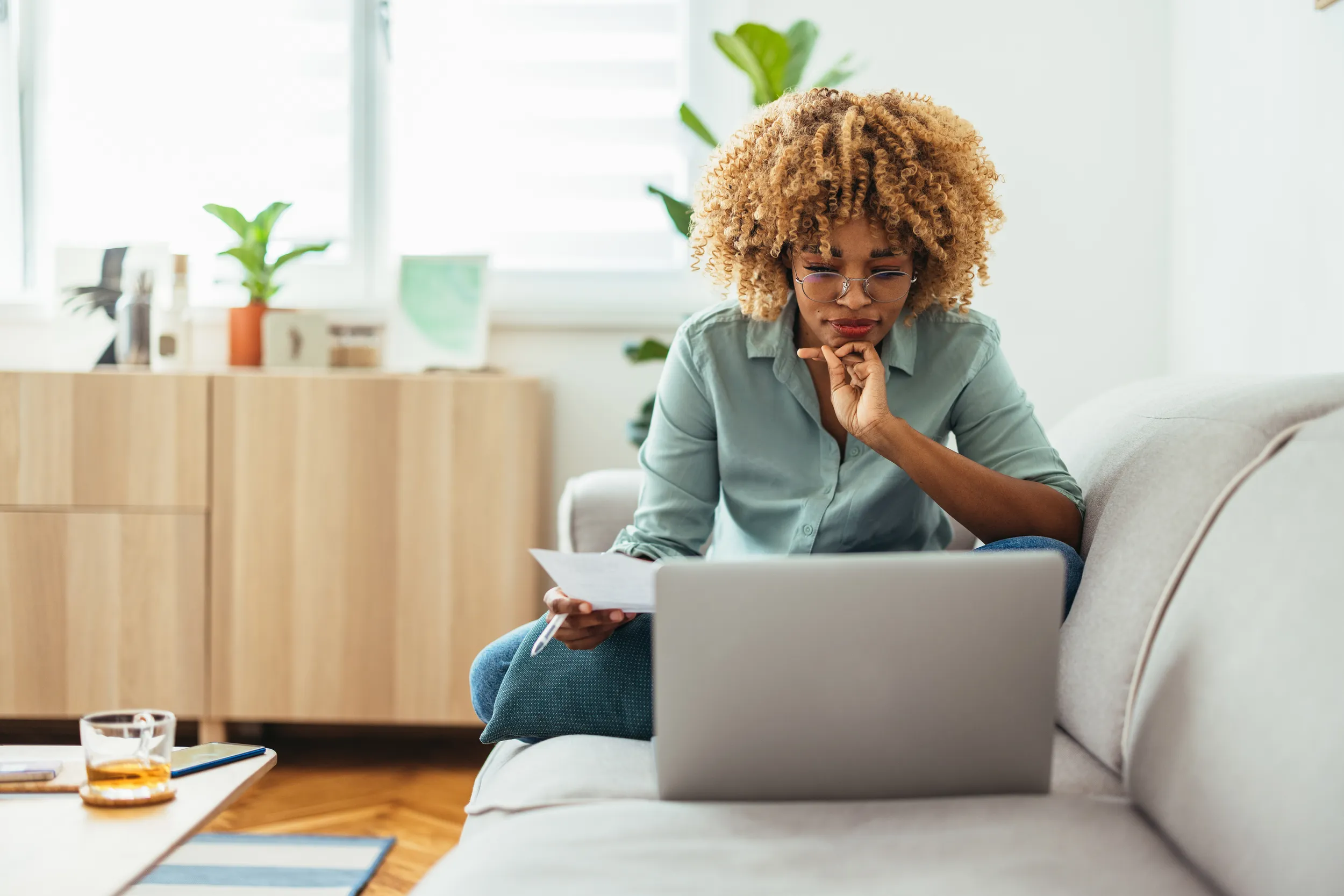 Black woman with blond hair sitting on her couch reading a laptop