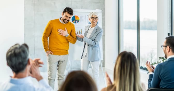 A guy in the foreground smiling with a woman presenting him.