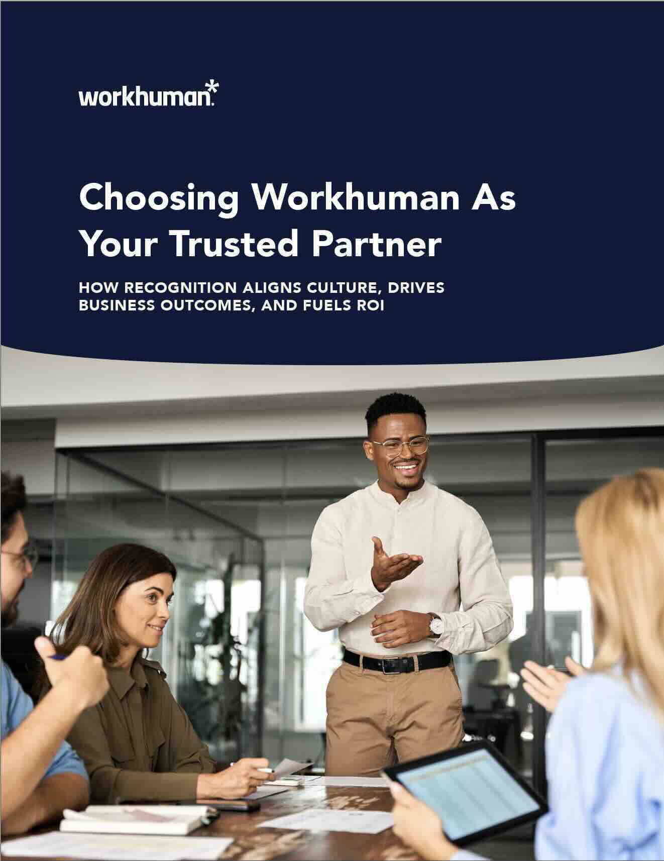 A business meeting in a modern office setting with a diverse group of four individuals seated around a table. A man standing and gesturing enthusiastically, wearing a light-colored button-up shirt and glasses, is speaking to the group. The text on the top of the image reads, "Choosing Workhuman As Your Trusted Partner" with the subtitle "HOW RECOGNITION ALIGNS CULTURE, DRIVES BUSINESS OUTCOMES, AND FUELS ROI." The atmosphere appears collaborative, with two individuals smiling and engaging in the conversation. The background features glass walls and greenery.