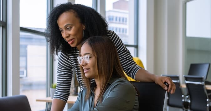 Two woman looking towards a computer.
