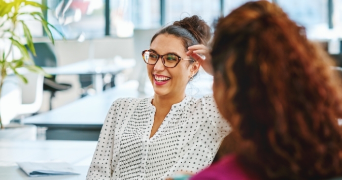 Two women in an office discussing employee of the month ideas for their program