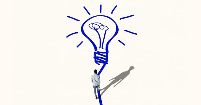 A person in a white shirt stands facing an oversized illustration of a light bulb drawn in blue on a light beige background. The bulb is stylized with rays extending outward, and a winding line leads from the person to the base of the bulb.