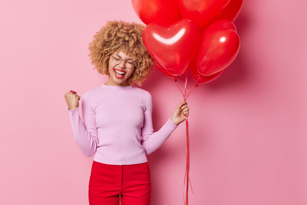Lady holding heart shaped balloons and looking happy