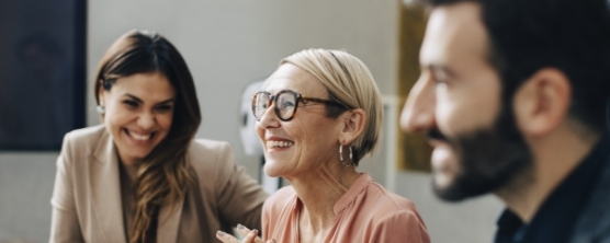 Three people smiling in a room. Older woman looking off to the left of the frame.