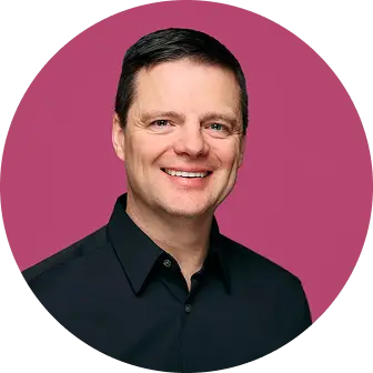 A man smiling, dressed in a black shirt, is featured against a vibrant pink background.